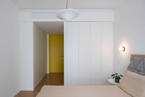 Modern minimalist bedroom interior with white walls, a white pendant light, and a yellow door in the background.