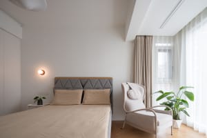 A minimalist bedroom with a comfortable bed, armchair, and large window with curtain.