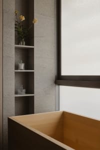 A minimalist bathroom featuring wooden shelves, a wooden bathtub, and a window with a white frame.
