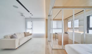 A modern living room with a neutral color palette featuring a comfortable sofa, blinds, and a study area with a desk and wind