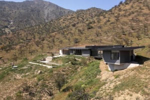 A modern holiday villa with glass walls overlooking a mountainous landscape.