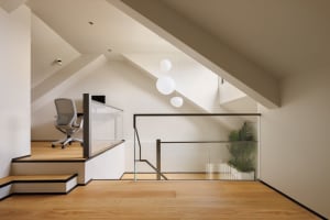 A modern home office with glass partitions, wooden floors, a white chair, and a hanging white light fixture.