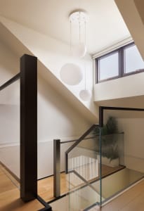 Modern interior with glass stair railing, steel accents, oak flooring, and a plant.