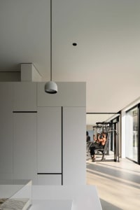 A minimalist home gym with concrete flooring and white cabinets, featuring a workout machine and a person exercising.