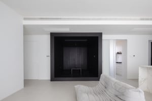 A modern minimalist living room with a black box feature wall, concrete floor, and white sofa.