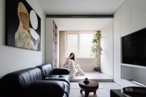 A modern minimalist living room featuring a black leather sofa, a round wooden table, and a large abstract painting on the wa