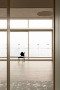 A minimalist residential interior featuring a solitary green chair positioned in front of a large window.