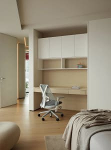 Modern minimalist master bedroom featuring a white desk with a mesh office chair, beige flooring, and light-colored wood cabi