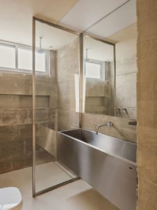 A minimalist bathroom with concrete walls, a stainless steel bathtub, and a glass shower enclosure with a white floor.