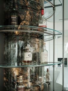 Glass shelves and bottles on a curved bar counter with a marble background.