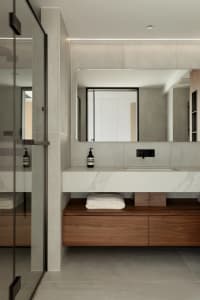 Modern minimalist bathroom with marble countertop and wooden storage, featuring a sleek sink, large mirror, and glass shower 