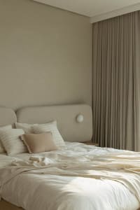 A minimalist bedroom with a bed dressed in neutral colors, including white sheets, a beige throw pillow, and a beige headboar