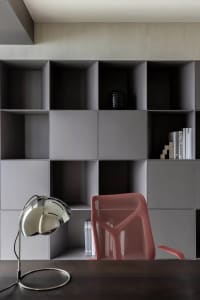 A minimalistic home office with concrete grey shelves, a red mesh office chair, a black desk lamp, and some books.