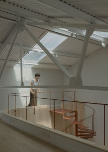 A person standing near a modern, minimalist interior with a spiral staircase made of metal.