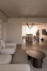 Modern minimalist living room with neutral tones, featuring a large sofa, a round coffee table, and a dining area in the back