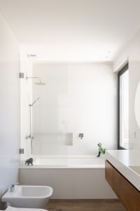 Modern minimalist bathroom with white tiled walls, a glass shower enclosure, a bathtub, and a wooden floor.