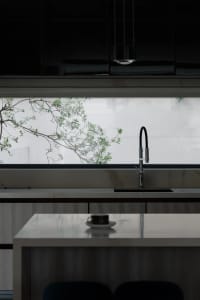 A modern, minimalist kitchen with a marble countertop and a view of greenery outside the window.