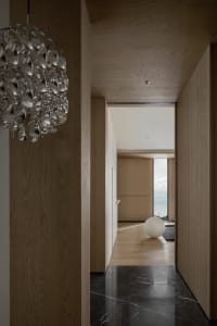 A modern minimalist hallway with polished wooden walls and a black marble floor. A modern chandelier hangs from the ceiling, 