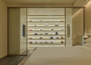 A sleek, minimalist bedroom features a glass-enclosed shoe collection displayed on shelves.