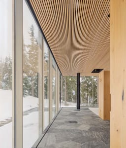 Modern interior corridor with glass walls, wooden ceiling panels, and stone flooring, featuring winter scenery with snow-cove