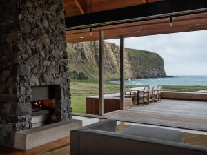 A modern coastal residence featuring a stone fireplace with a living area and outdoor deck overlooking the ocean.