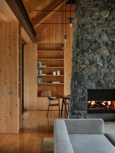 Modern minimalist living room featuring a cozy stone fireplace, wooden shelves, and a comfortable sofa.