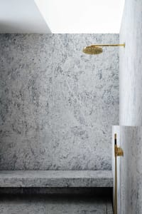 A minimalist bathroom featuring granite walls and a brass shower head