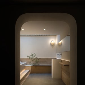 A minimalist bathroom with wooden accents and concrete elements, featuring a tub, sink, and wall-mounted lights.