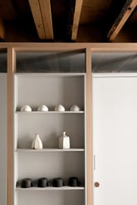 A white wooden bookshelf with two shelves holding various ceramic vases and cups.