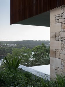 A modern exterior featuring stone walls and concrete patio overlooking lush greenery and distant hills.