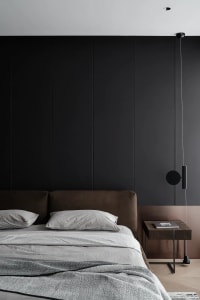 Modern minimalist bedroom with a textured fabric headboard and gray bedding against a dark accent wall.
