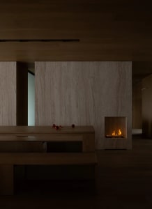 A modern living room with wood floors, taupe marble walls and a fireplace emitting a warm glow.