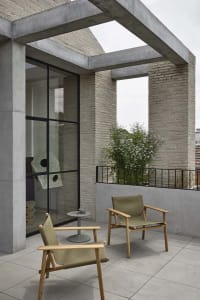 A minimalist balcony features concrete walls and a skylight, with two green canvas chairs and a small table.