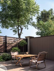 Outdoor teak dining table and chairs under a tree in a minimalist backyard.