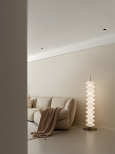 A minimalist living room with a beige sofa, neutral-toned floor lamp, and white walls.