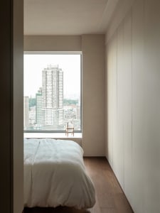 Modern minimalist bedroom with a wooden platform bed, overlooking a cityscape through a large window.