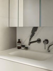 A modern bathroom featuring a white marble countertop and sink, minimalist design, and sleek, dark fixtures.