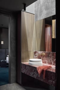 Modern minimalist bathroom featuring a white sink basin with a gold faucet, set against red marble and surrounded by sleek, d