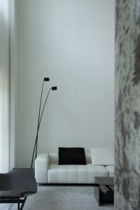 A minimalist living room featuring a white leather sofa with a black throw pillow, a marble side table, and a floor lamp with
