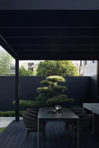 A modern outdoor dining area featuring a dark wooden deck with a black pergola and a black table surrounded by black chairs, 
