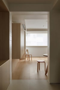 A minimalist living room featuring wooden flooring, a white chair, and a small table.