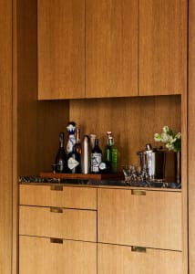 A modern home bar with wooden cabinets and shelves storing various bottles of liquor and glasses.