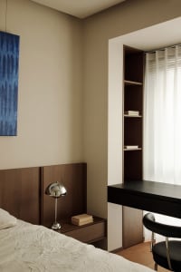 A modern minimalist bedroom with a wooden headboard, metal table lamp, and fabric sheets.