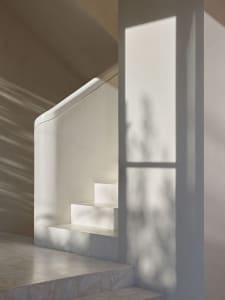 Modern staircase with marble steps and concrete wall, featuring light filtering through a window.