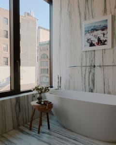 A minimalist bathroom with a freestanding bathtub, marble floor and walls, and framed photograph.