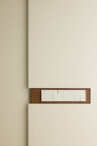 A minimalist light switch panel with a wooden frame and white plastic buttons mounted on a beige wall.