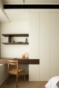 A minimalist bedroom with a wooden chair, white desk lamp, and white bookshelf.
