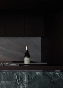 A modern kitchen featuring marble countertops and dark cabinets with a bottle of Moula Chardonnay.