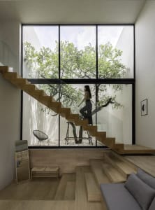 A modern staircase with wooden steps and a glass railing is prominent in a well-lit, contemporary interior space with a large