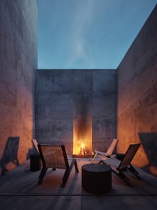 Minimalist outdoor living space featuring concrete walls and a fire pit.